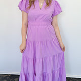 Maxi length dress with v neckline. Short sleeve with slightly bubbled sleeves. Tiered bottom. Elastic waist. Purple in color.
