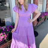 Maxi length dress with v neckline. Short sleeve with slightly bubbled sleeves. Tiered bottom. Elastic waist. Purple in color.