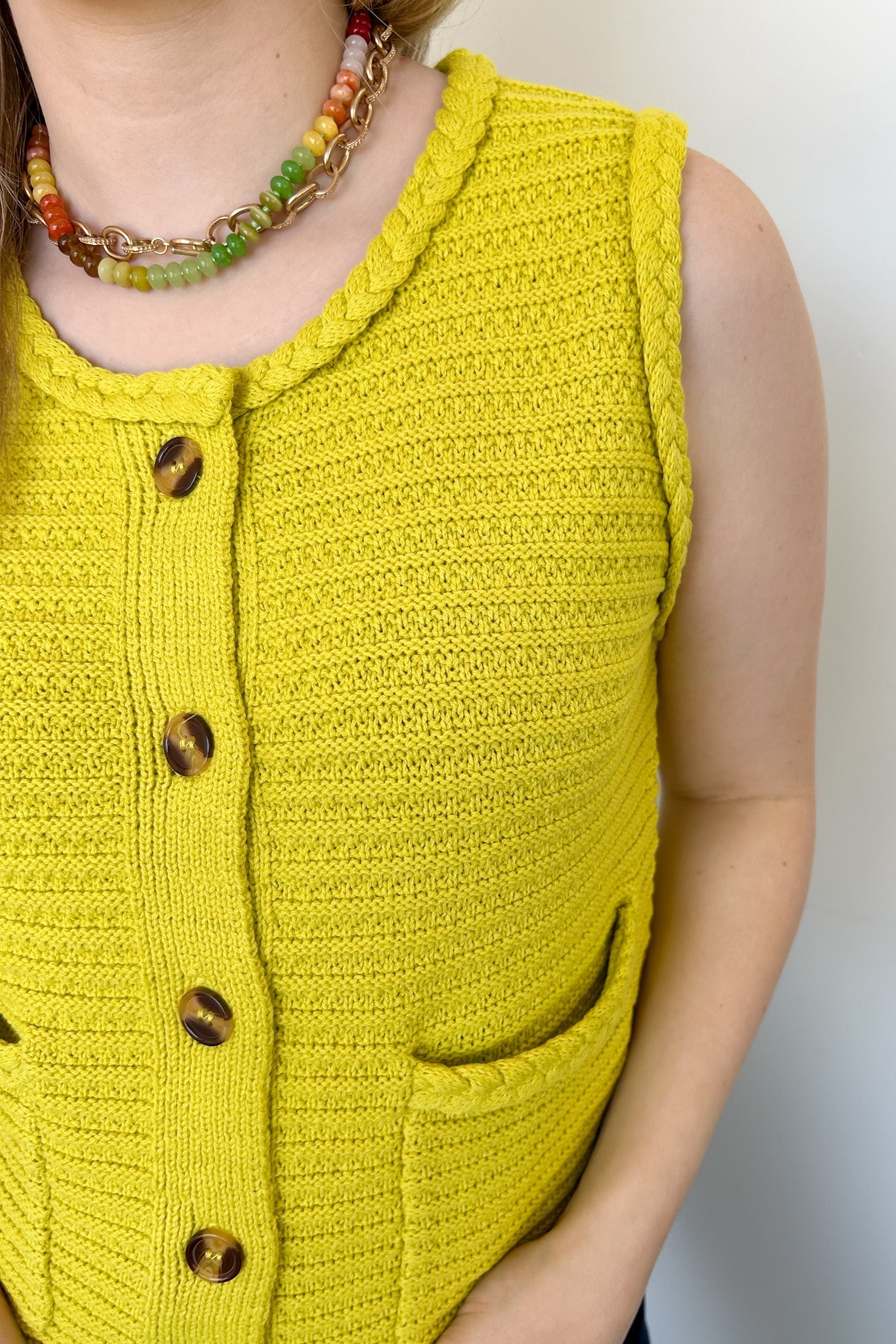 Button up vest with brown buttons. Pockets in the front. Braided detail around the tank sleeves and neckline, as well as the bottom of the top. Chartreuse in color.