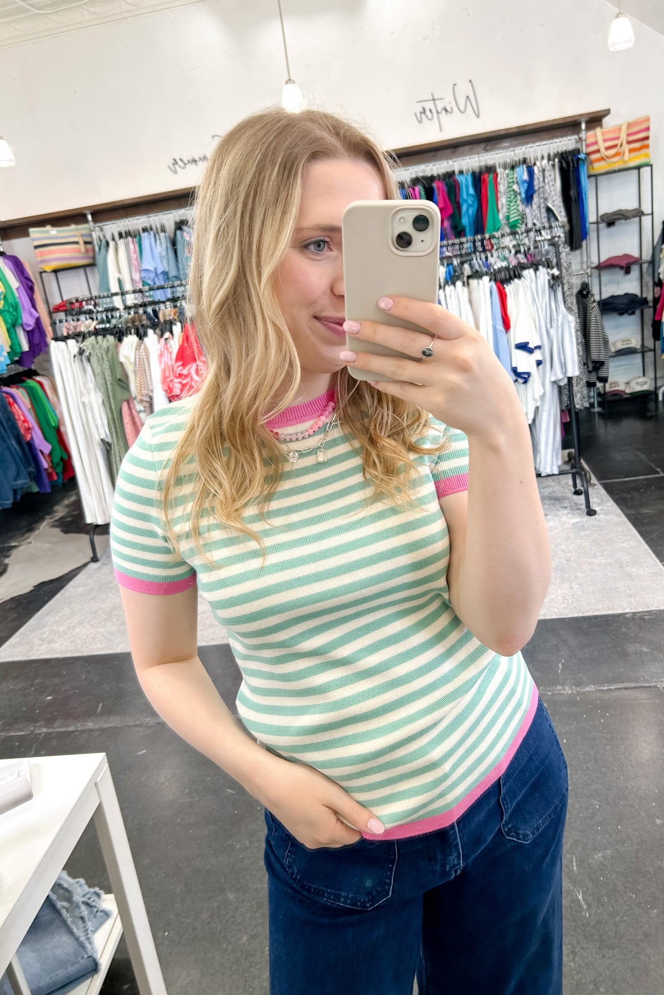 Striped top in a mint blue color with pink lining the neckline and around the short sleeves, as well as along the bottom. High neckline and slightly fitted style.