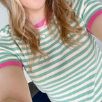 Striped top in a mint blue color with pink lining the neckline and around the short sleeves, as well as along the bottom. High neckline and slightly fitted style.