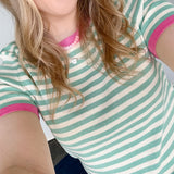 Striped top in a mint blue color with pink lining the neckline and around the short sleeves, as well as along the bottom. High neckline and slightly fitted style.