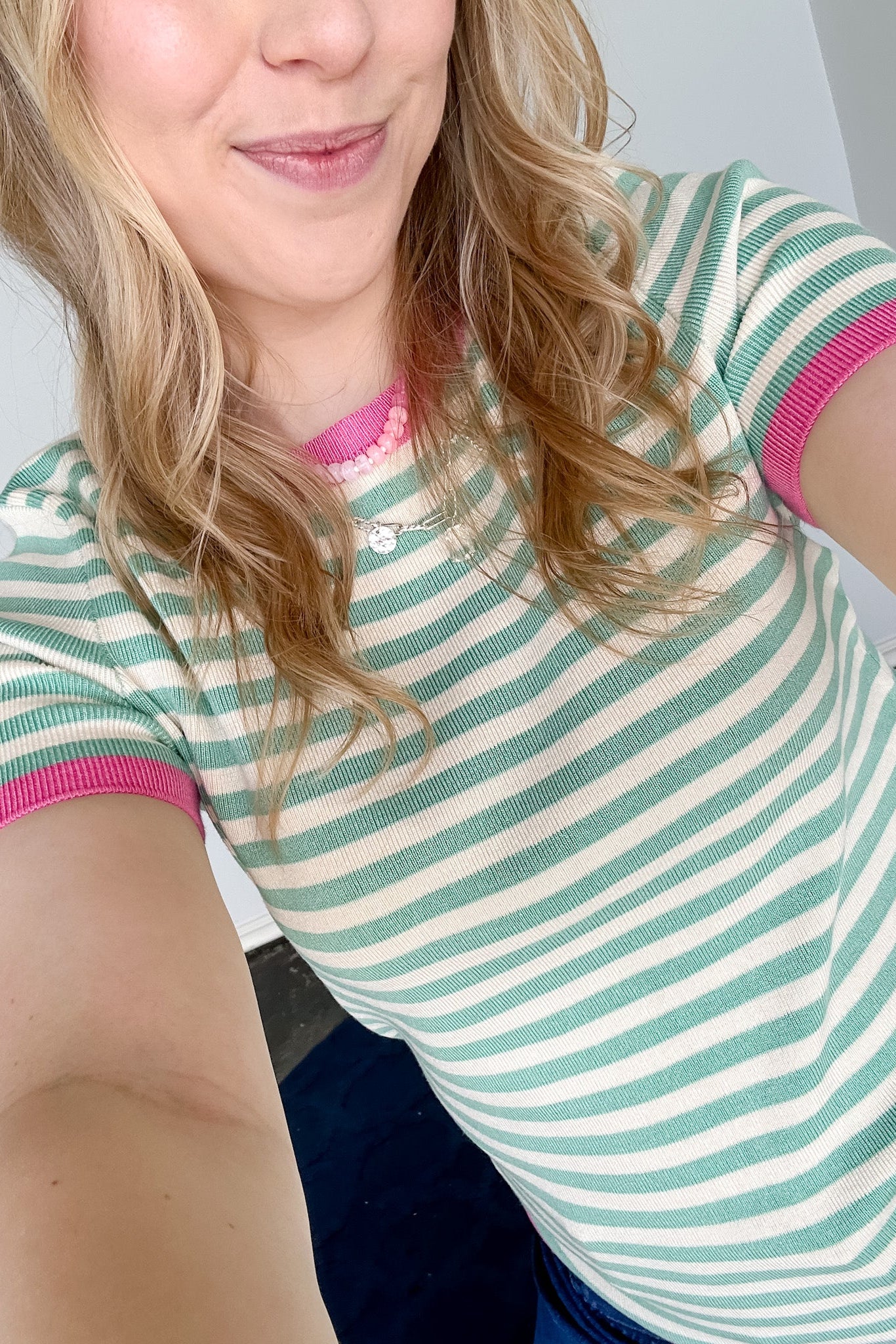 Striped top in a mint blue color with pink lining the neckline and around the short sleeves, as well as along the bottom. High neckline and slightly fitted style.