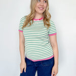Striped top in a mint blue color with pink lining the neckline and around the short sleeves, as well as along the bottom. High neckline and slightly fitted style.