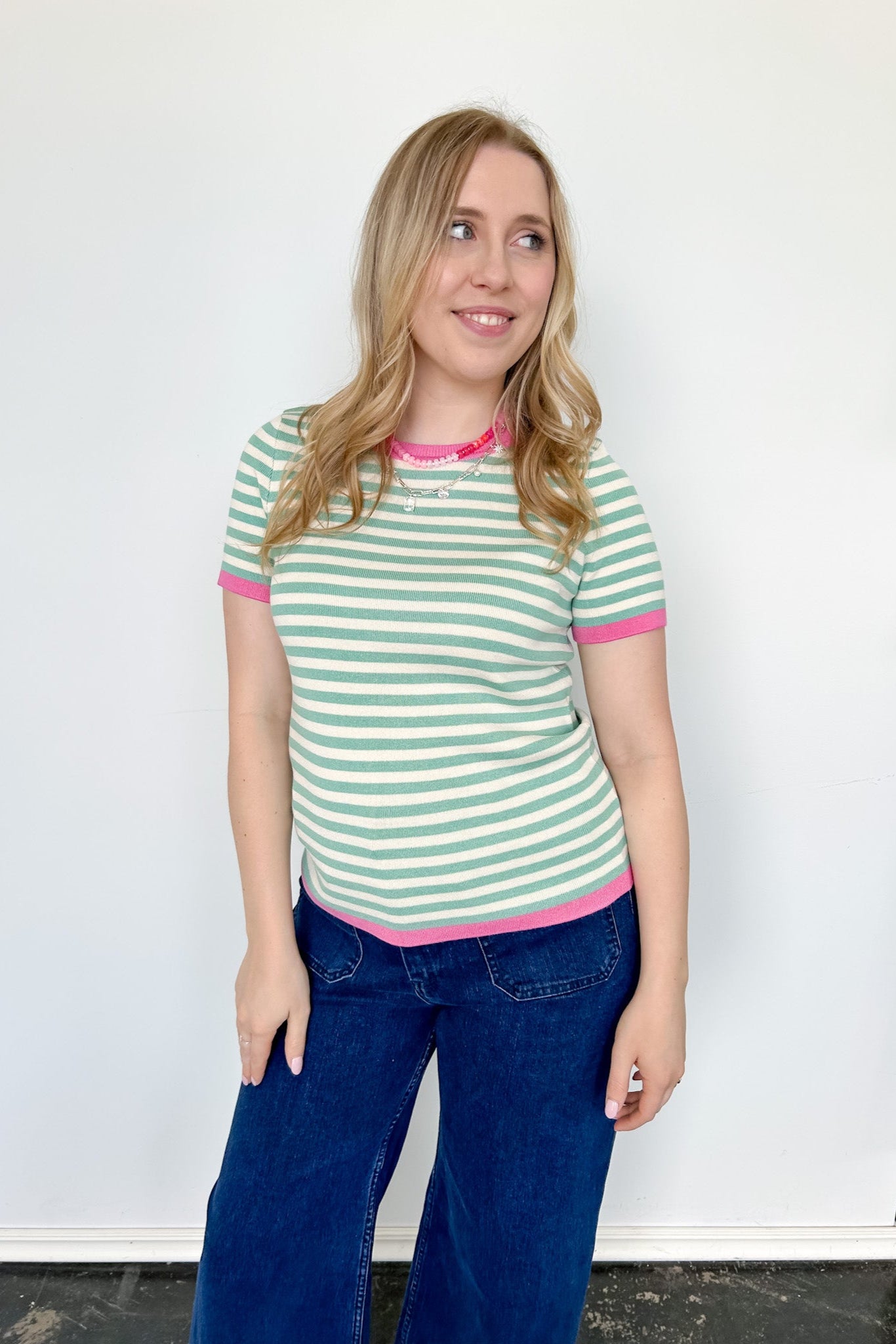Striped top in a mint blue color with pink lining the neckline and around the short sleeves, as well as along the bottom. High neckline and slightly fitted style.
