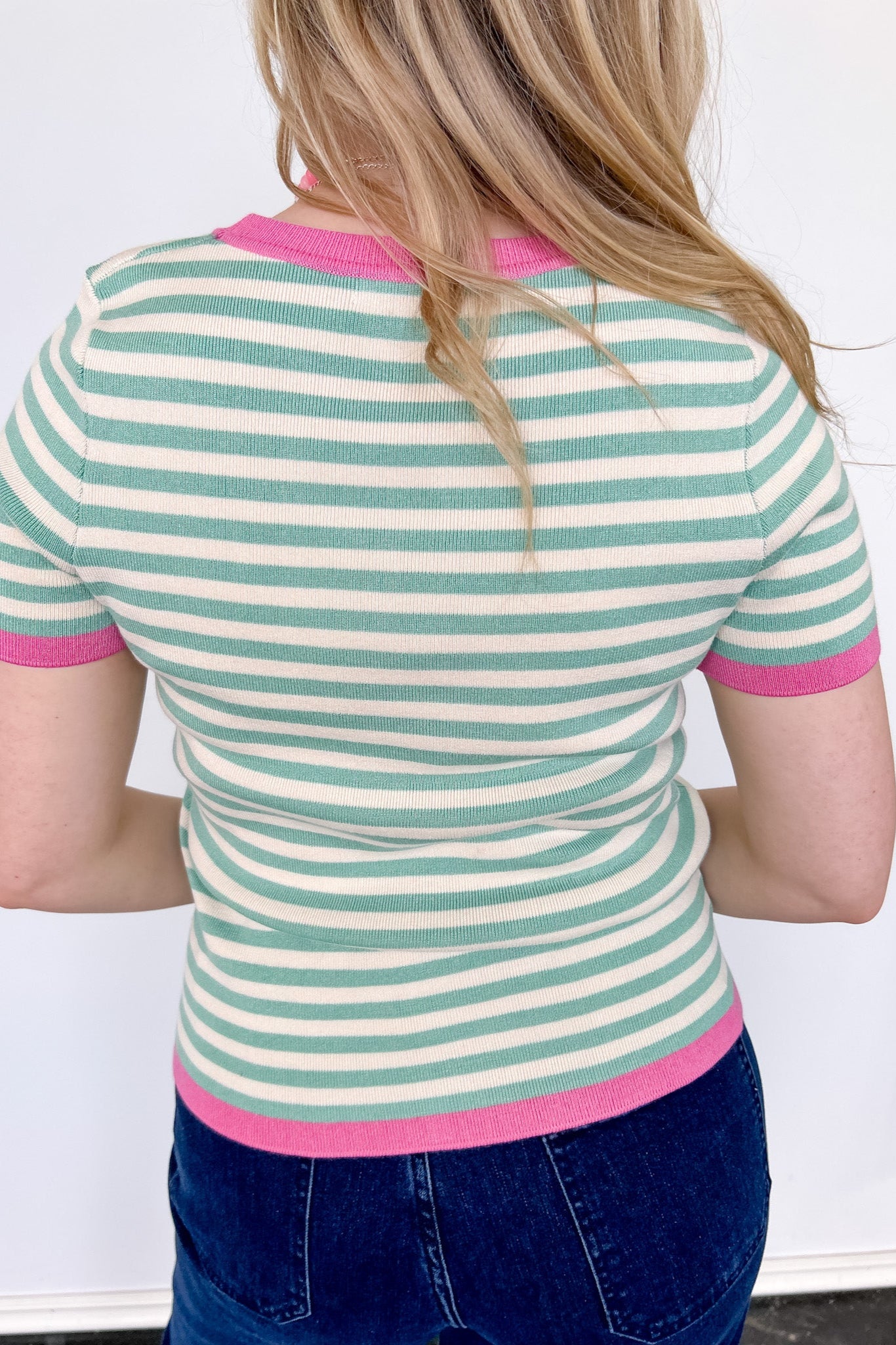 Striped top in a mint blue color with pink lining the neckline and around the short sleeves, as well as along the bottom. High neckline and slightly fitted style.