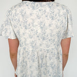 Short flowy sleeved top with button detailing. Cream in color with light blue floral pattern. Babydoll style.