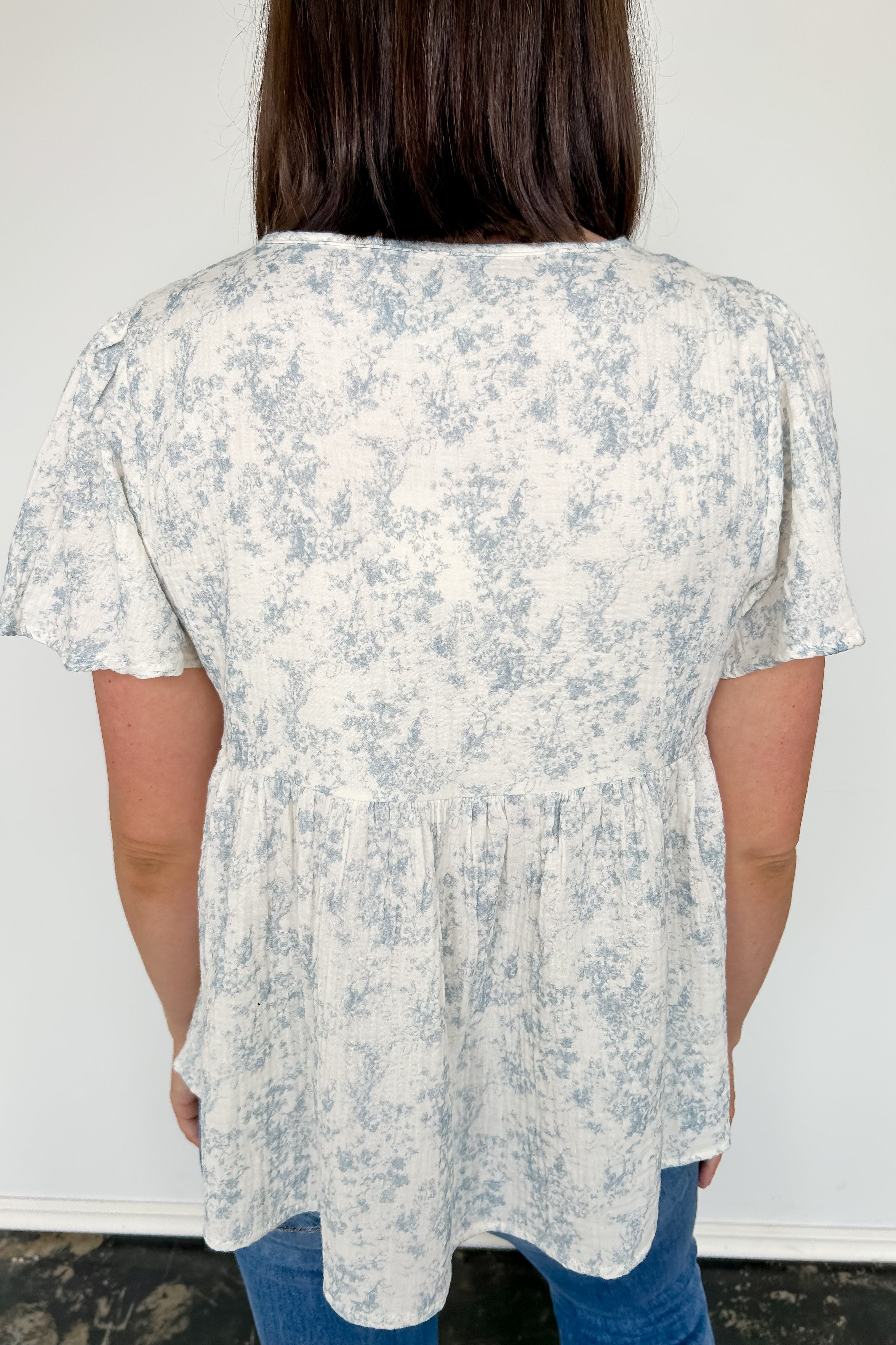Short flowy sleeved top with button detailing. Cream in color with light blue floral pattern. Babydoll style.