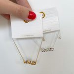 Gold bracelet with 'WWJD' pendant held by a hand with red nail polish on a white background