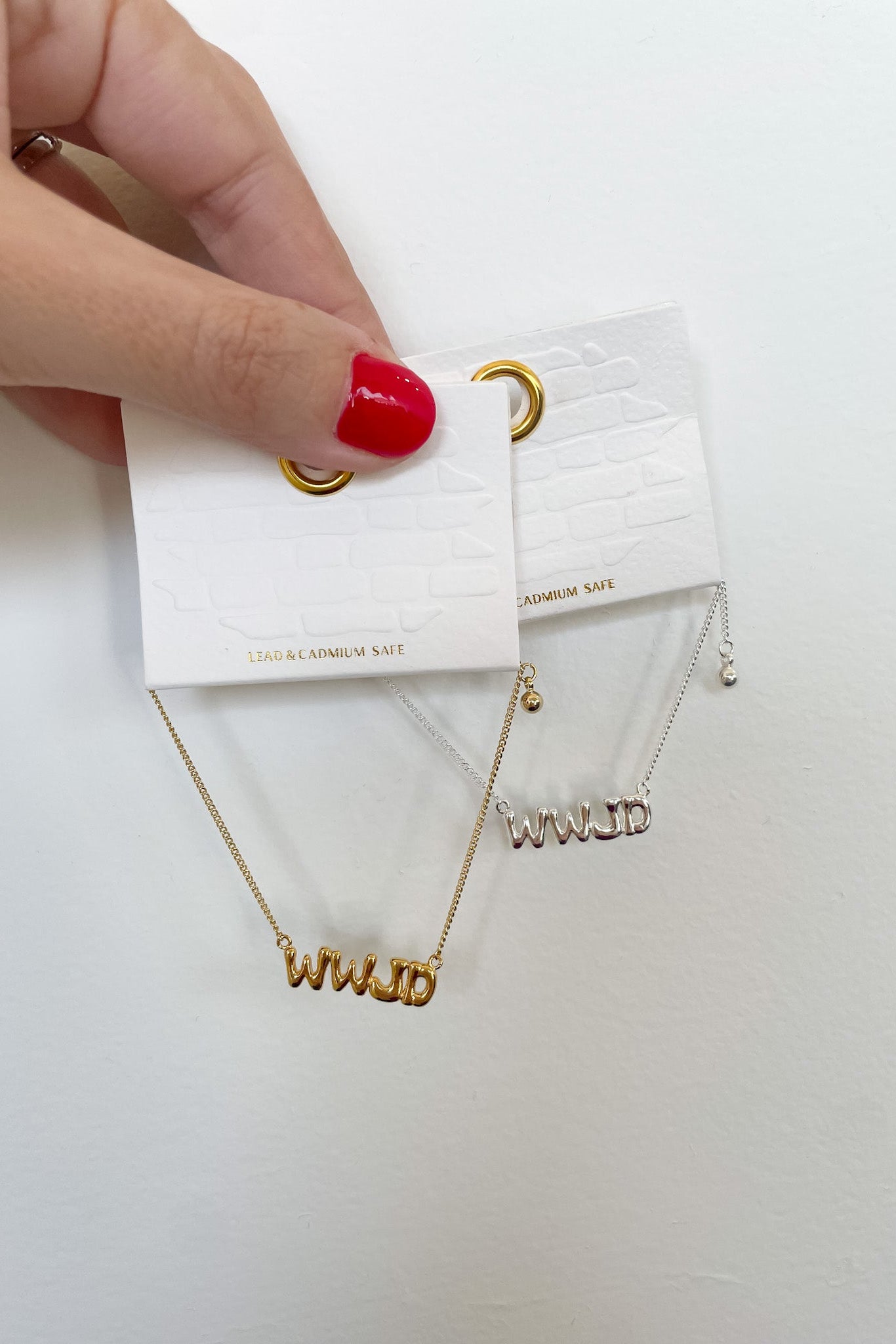 Gold bracelet with 'WWJD' pendant held by a hand with red nail polish on a white background