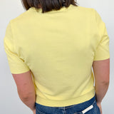 Person wearing a yellow top and blue jeans against a white wall