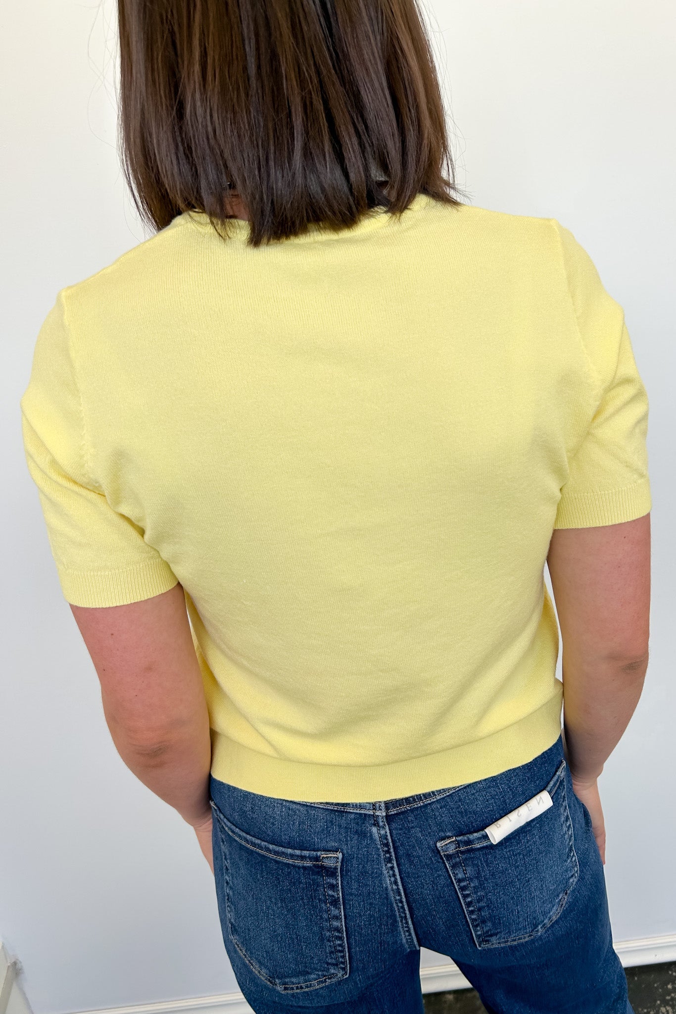 Person wearing a yellow top and blue jeans against a white wall