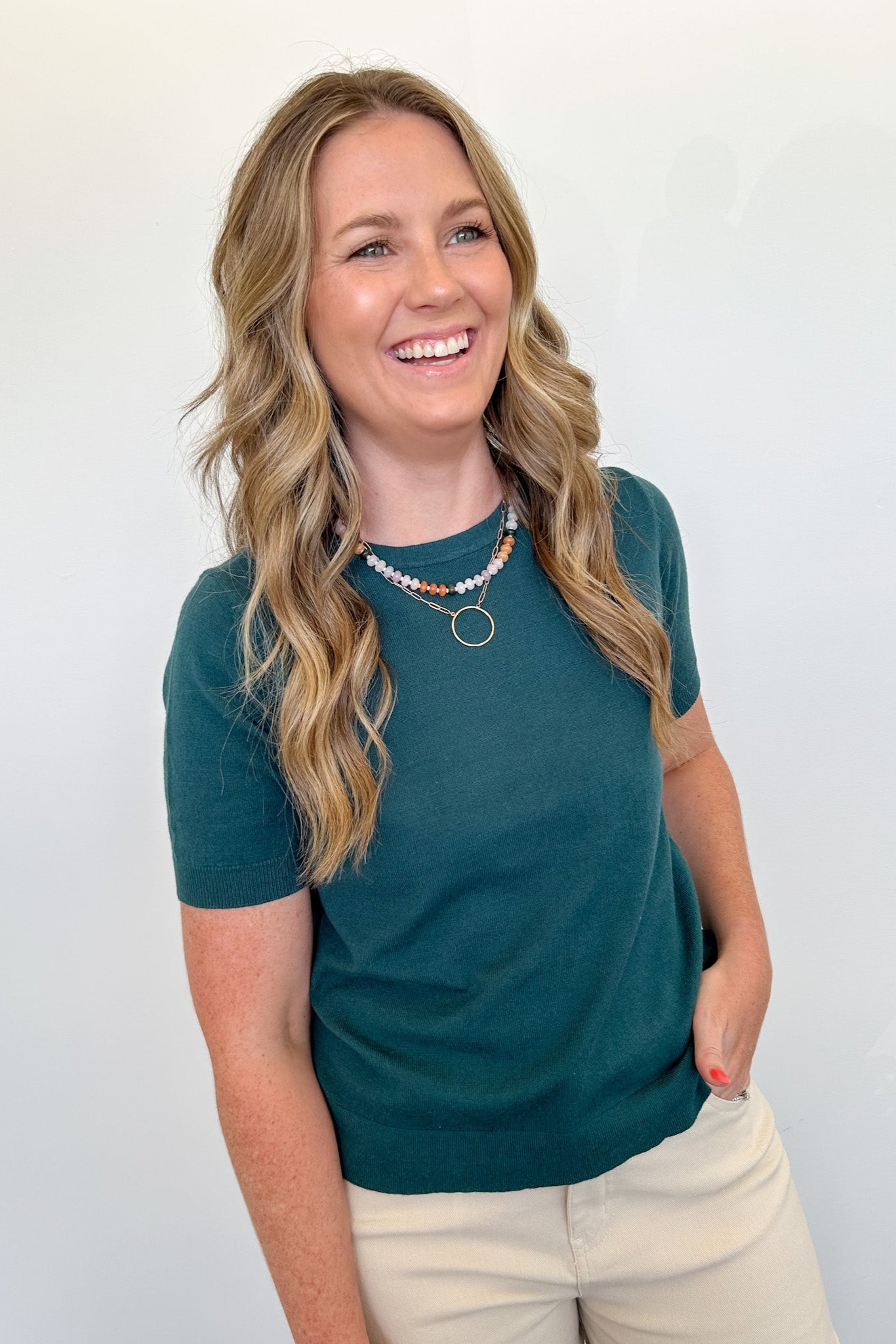Woman wearing a teal shirt and beige pants against a white background
