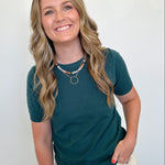 Woman wearing a teal shirt and beige pants against a white wall