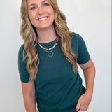 Woman wearing a teal shirt and beige pants against a white wall