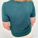 Person wearing a teal shirt and beige pants against a white wall