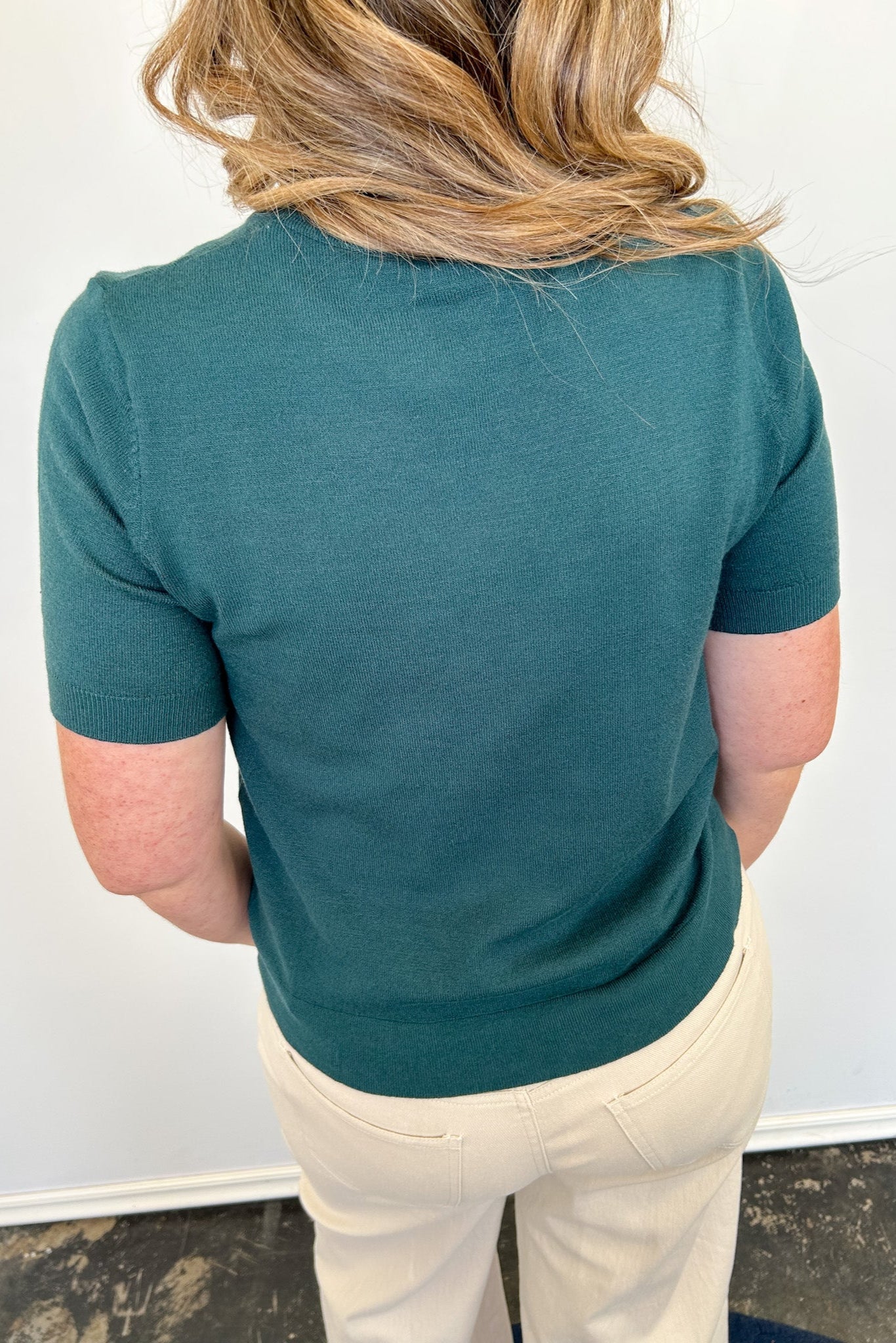 Person wearing a teal shirt and beige pants against a white wall