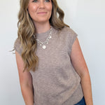 Woman wearing a brown sleeveless top and blue jeans against a white background