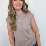 Woman wearing a brown sleeveless top and blue jeans against a white background