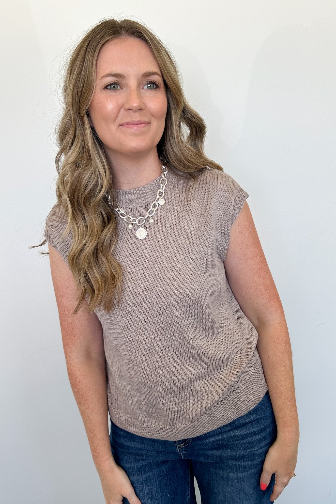 Woman wearing a brown sleeveless top and blue jeans against a white background