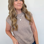 Woman wearing a beige sleeveless top and blue jeans against a white background