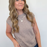 Woman wearing a beige sleeveless top and blue jeans against a white background