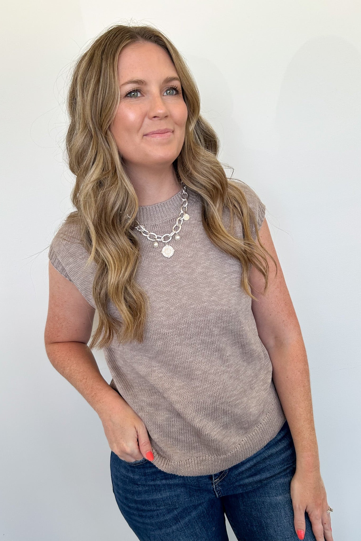 Woman wearing a beige sleeveless top and blue jeans against a white background