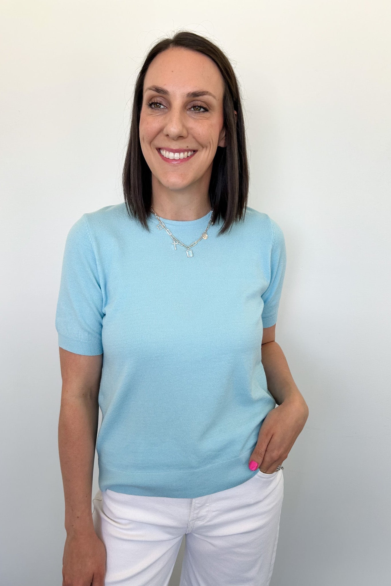 Woman wearing a light blue sweater and white pants against a plain background