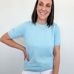 Woman wearing a light blue shirt and white pants against a plain background