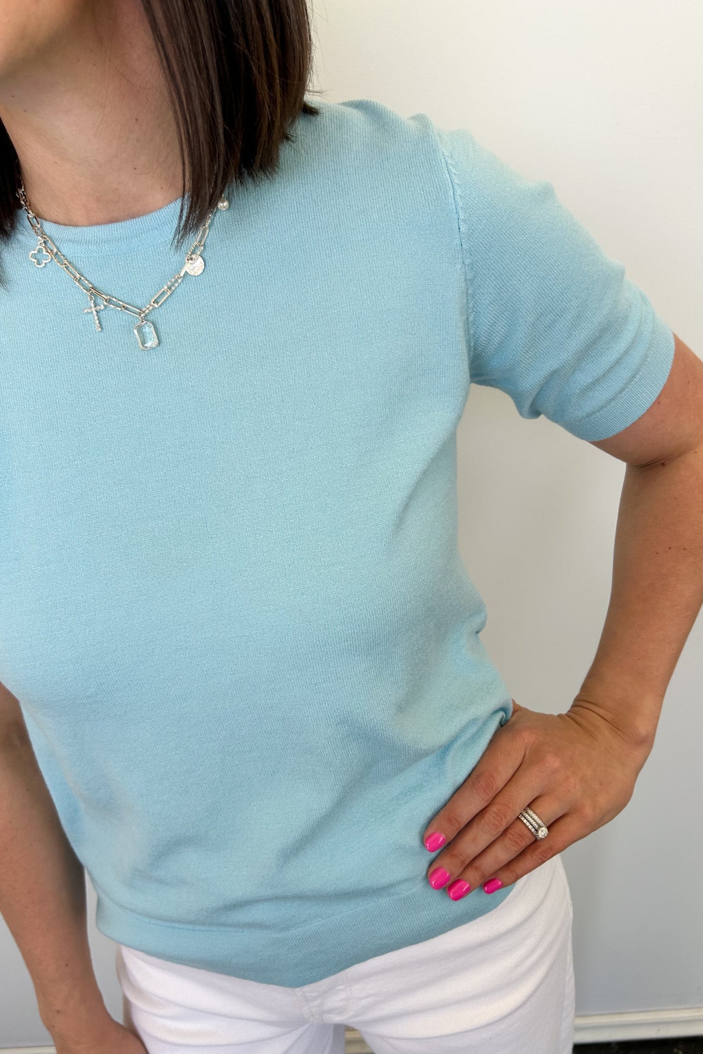 Woman wearing a light blue sweater and white pants against a plain background