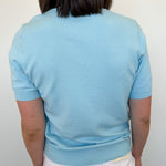 Person wearing a light blue sweater and white pants against a plain background