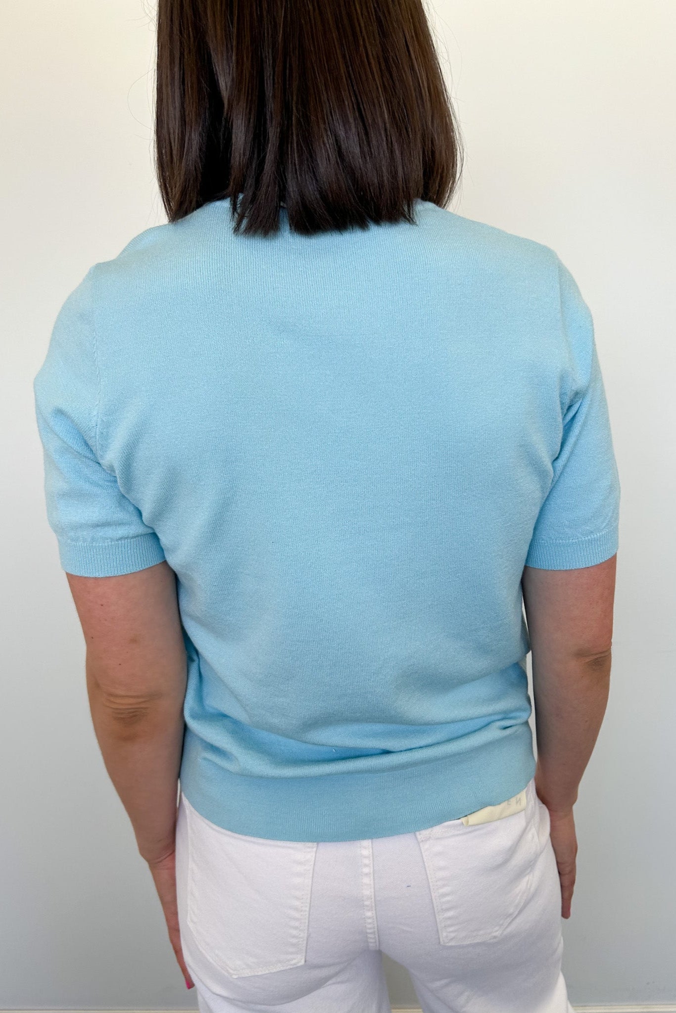 Person wearing a light blue sweater and white pants against a plain background