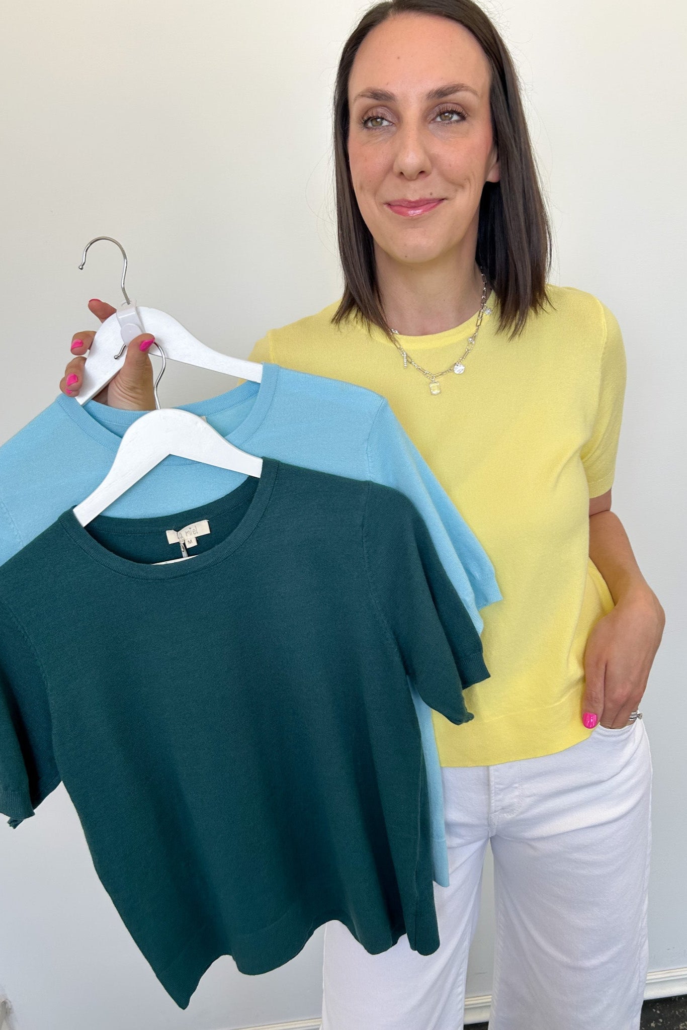 Woman holding two shirts on a hanger against a white background