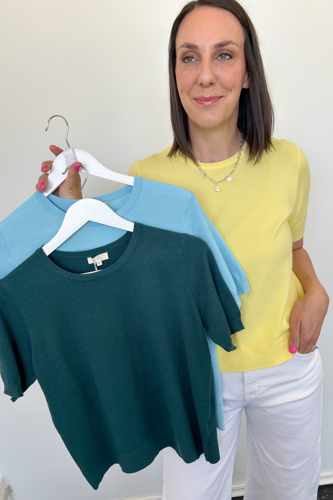Woman holding two shirts on a hanger against a white background