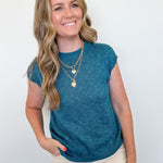 Woman wearing a teal sleeveless top with beige pants against a white background