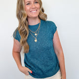 Woman wearing a teal sleeveless top with beige pants against a white background