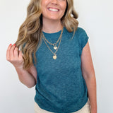Woman wearing a teal sleeveless top with beige pants against a white background