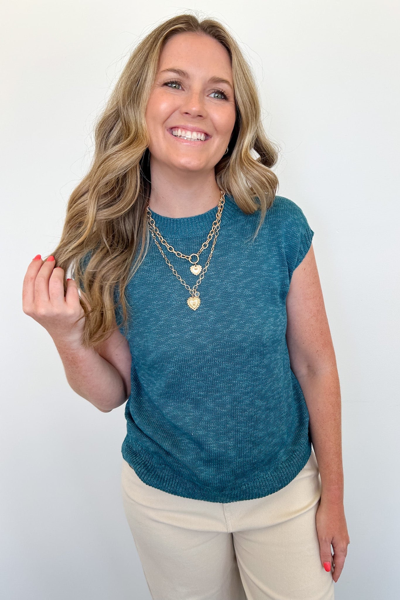 Woman wearing a teal sleeveless top with beige pants against a white background