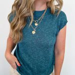 Woman wearing a teal top and beige pants with a white background