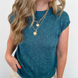 Woman wearing a teal top and beige pants with a white background