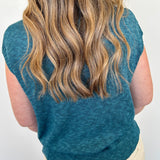 Person wearing a teal sleeveless sweater against a white background