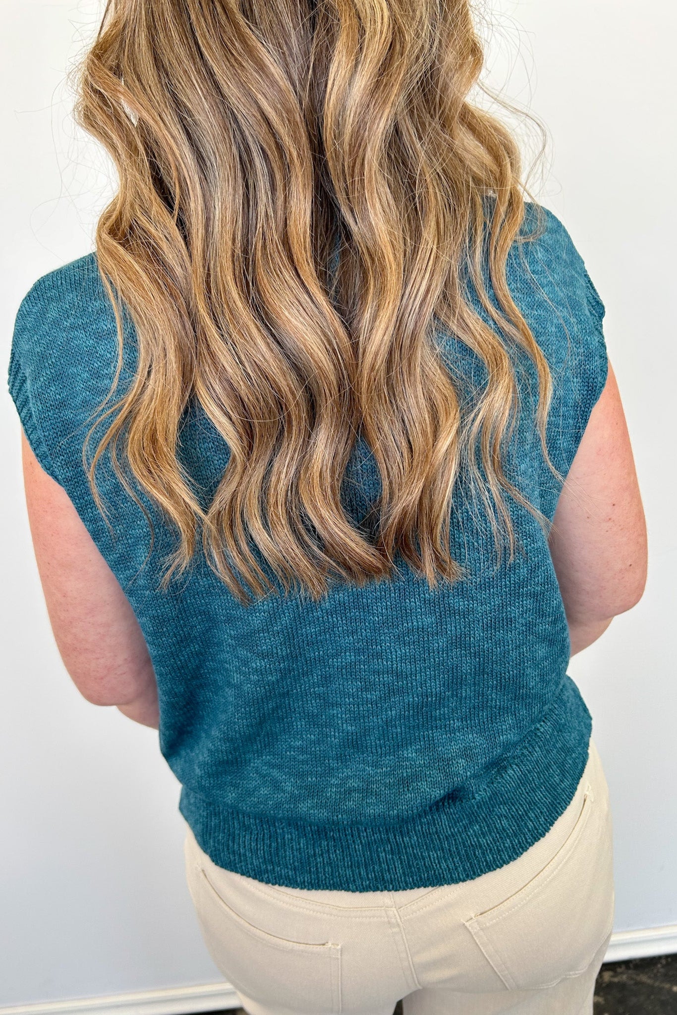 Person wearing a teal sleeveless sweater against a white background