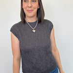Woman wearing a dark gray sleeveless top and blue jeans against a plain background