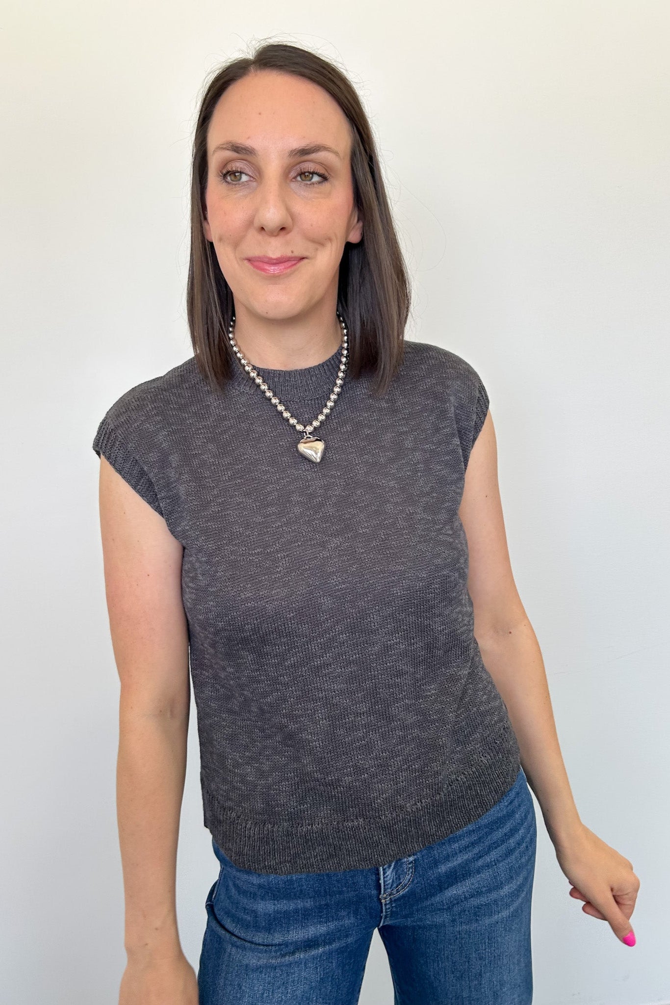 Woman wearing a dark gray sleeveless top and blue jeans against a plain background