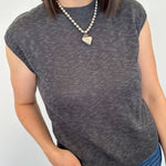 Person wearing a gray sleeveless top and blue jeans with a white background