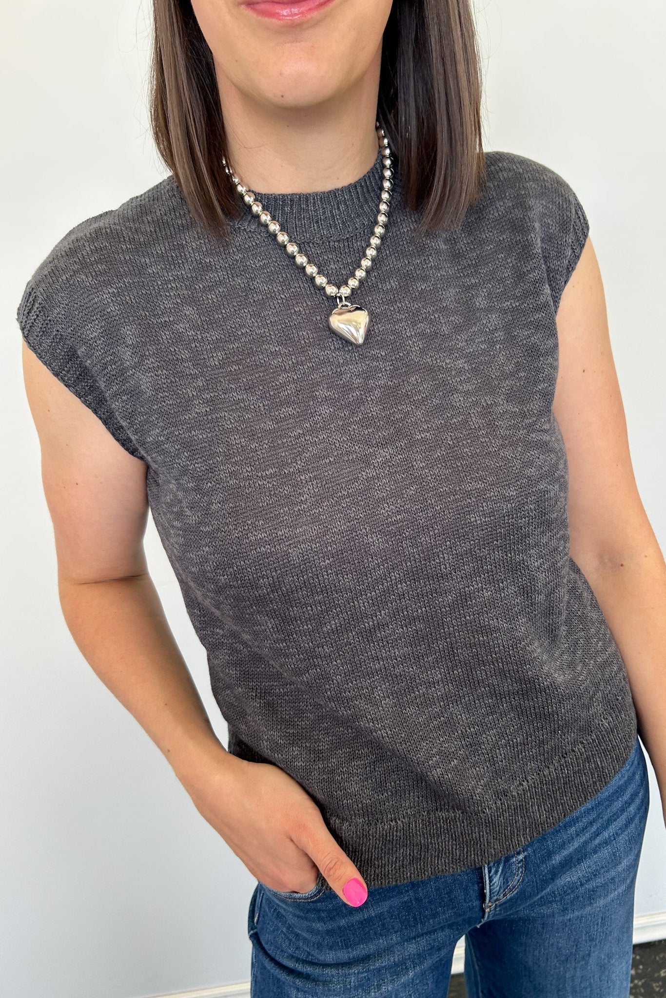 Person wearing a gray sleeveless top and blue jeans with a white background