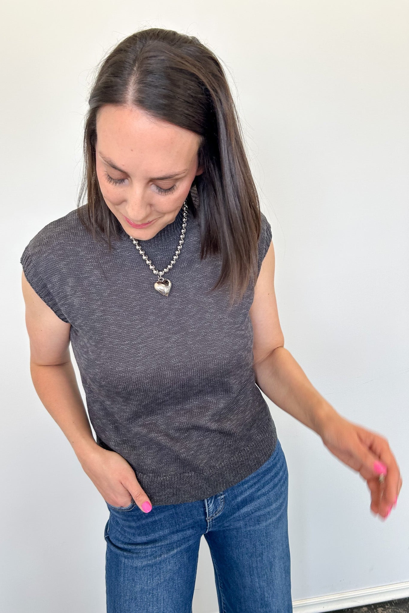 Woman wearing a gray sleeveless top and blue jeans against a white background
