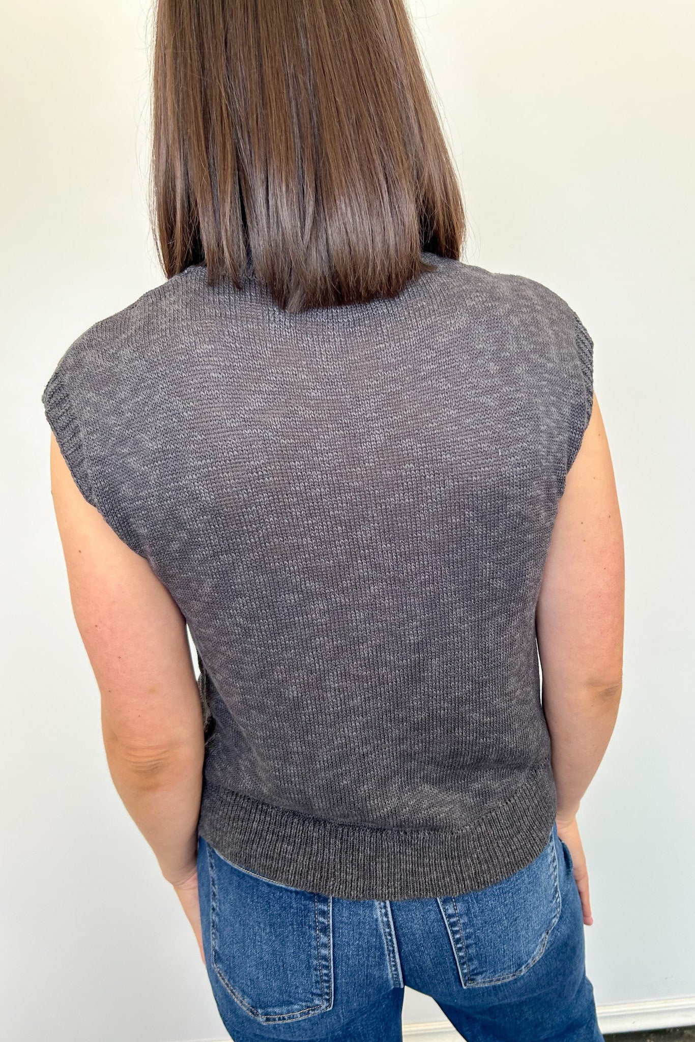 Person wearing a gray sleeveless sweater against a white background