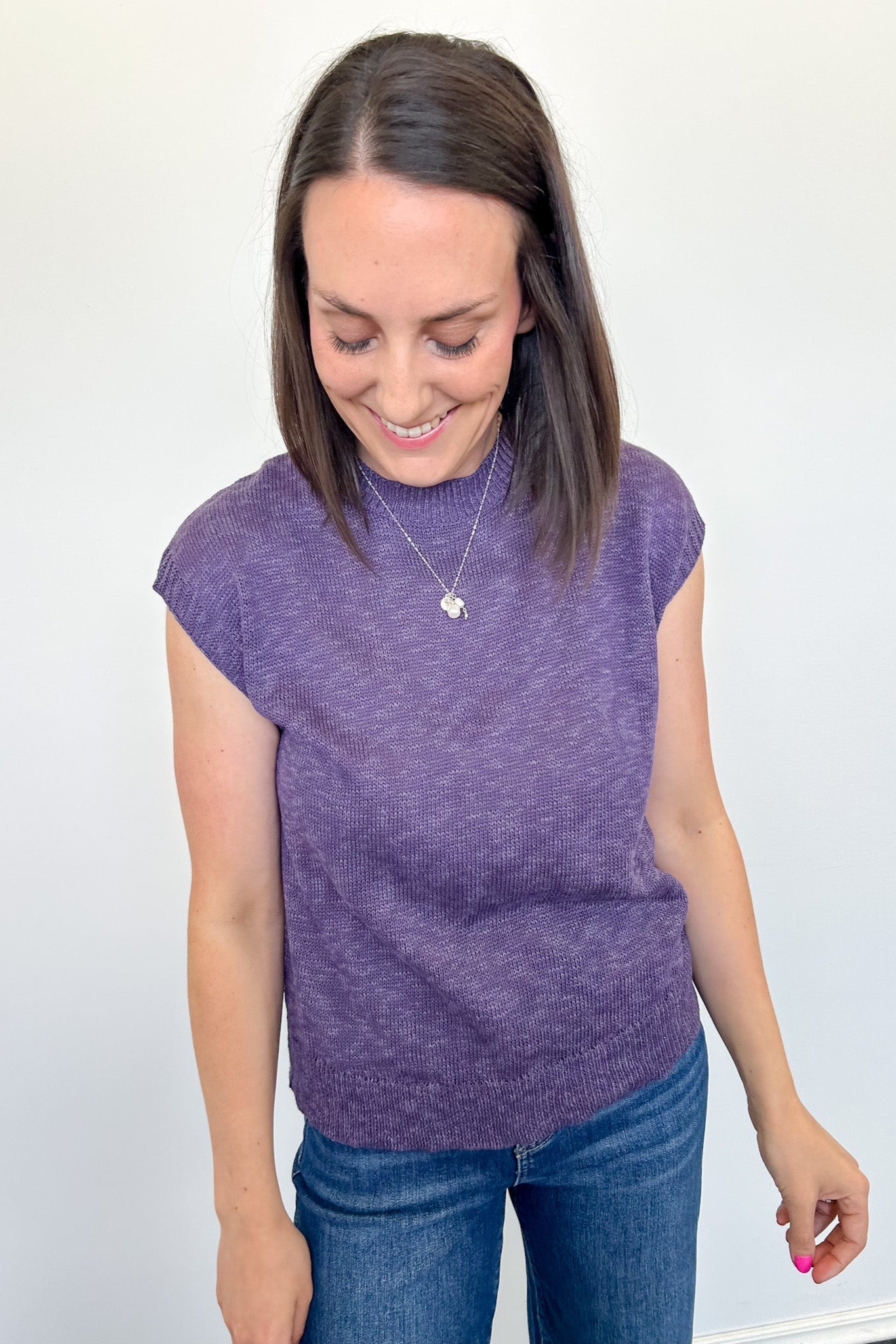 Woman wearing a deep summer purple sleeveless sweater against a white background
