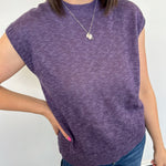 Person wearing a purple sleeveless sweater and blue jeans against a white background